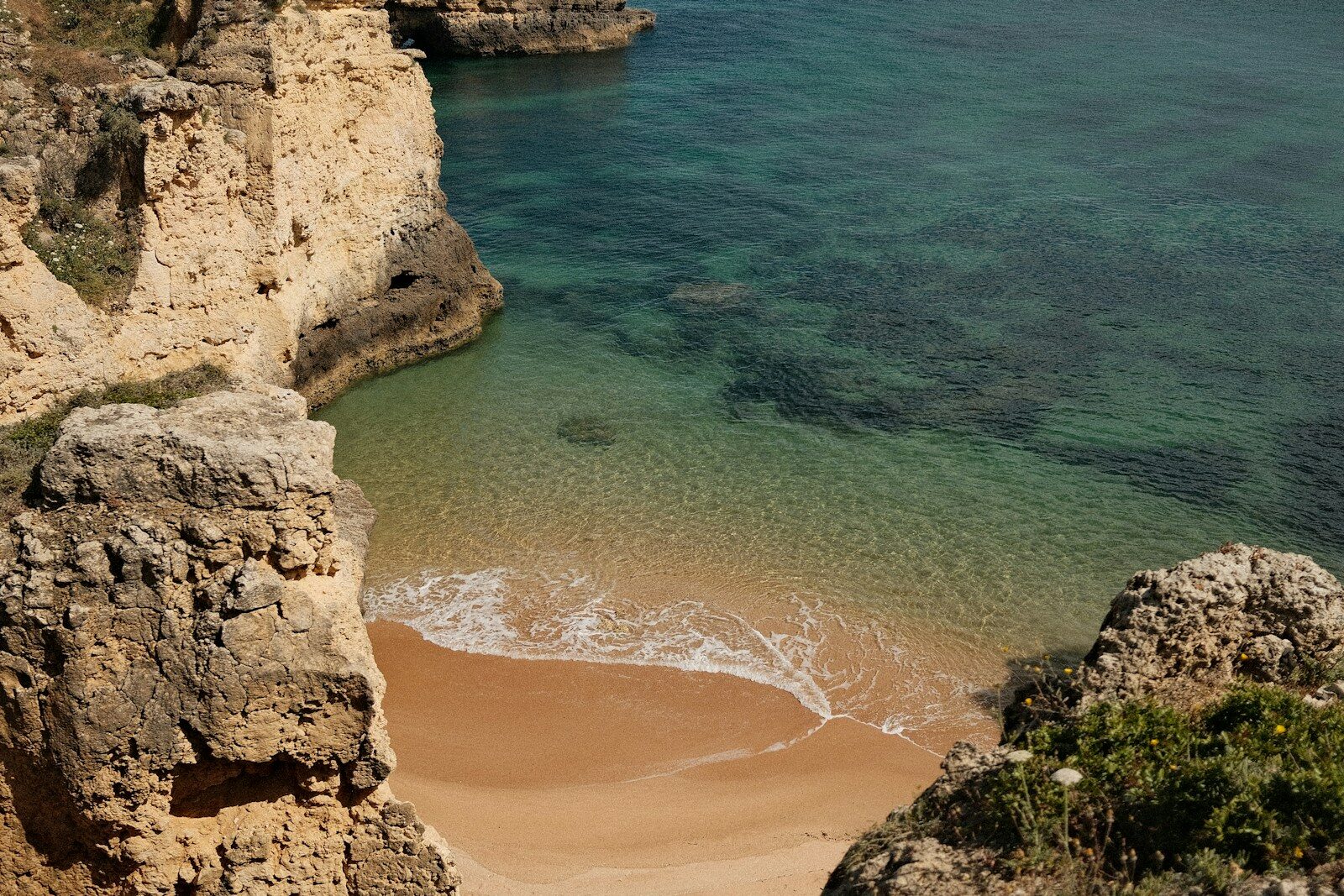 Secluded sandy cove with clear turquoise water and rocky cliffs.